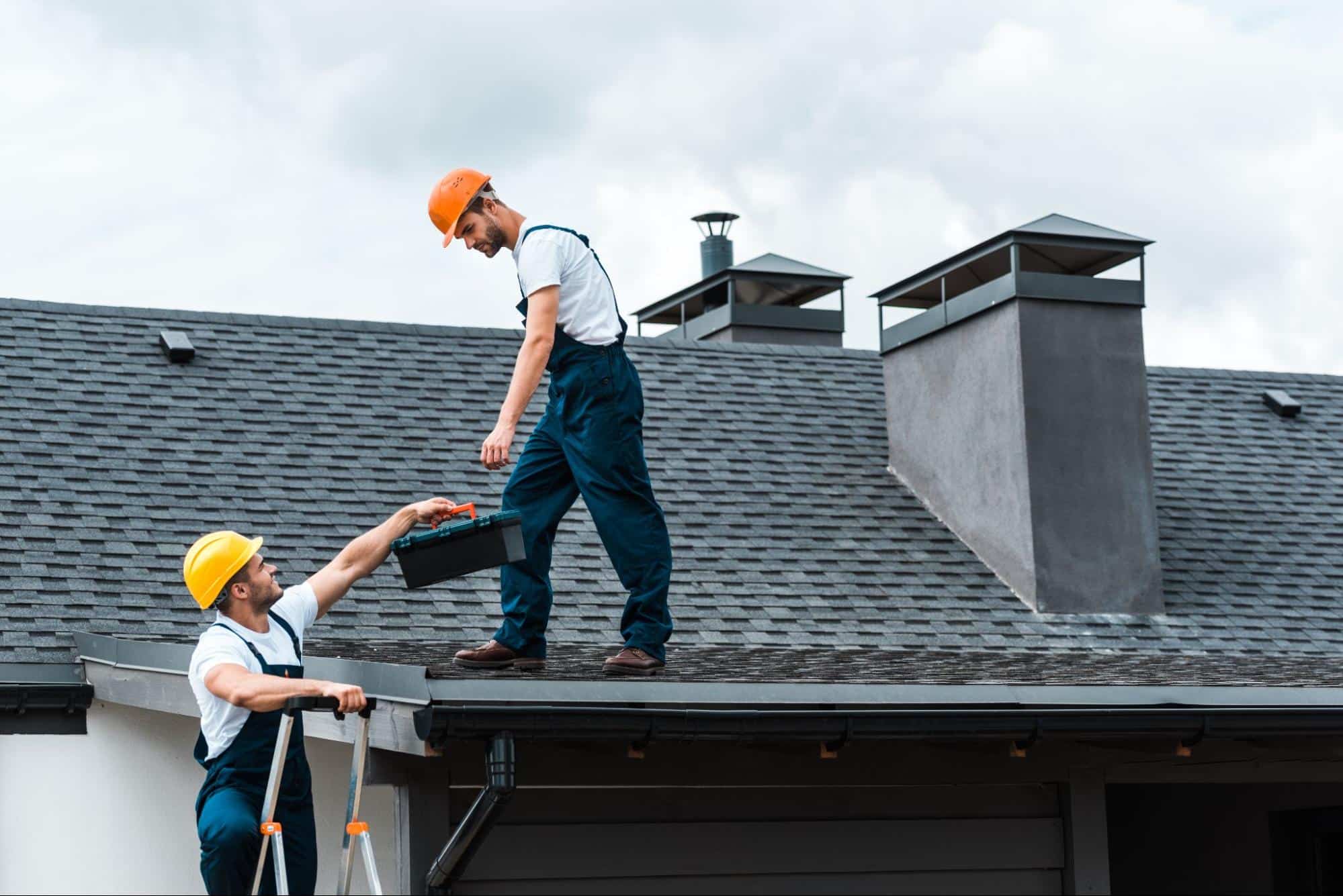 Workers in hard hats and overalls performing roofing services.