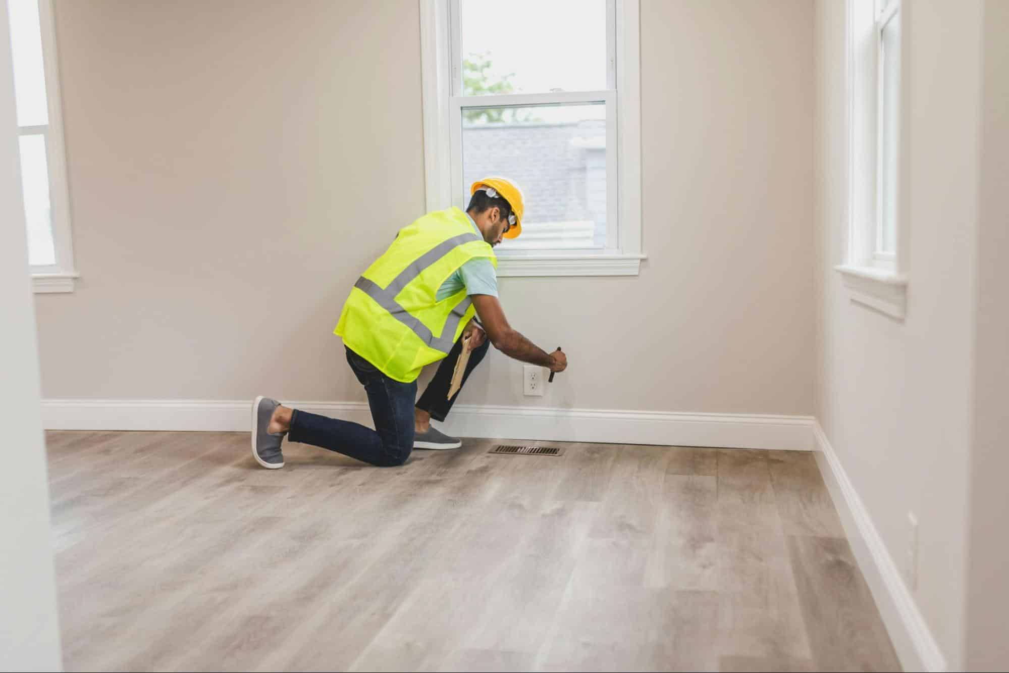 man in vest and hard hat inspecting house