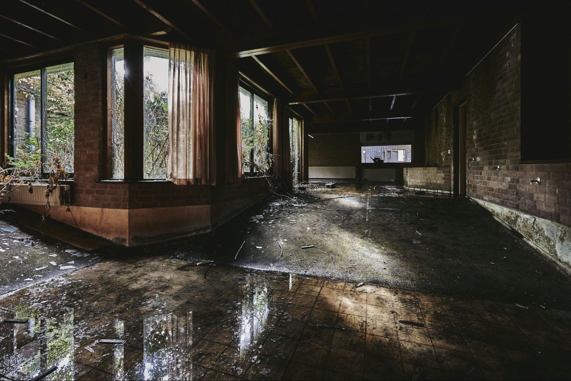 A dark, abandoned room with water pooling on the floor, visible mold on walls, and damaged surfaces, highlighting severe water damage requiring restoration.